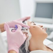 Beauty specialist with gloved hands holding a syringe and applying rejuvenation liquid in female cheek